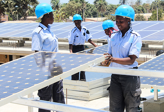 A group of 4 Black women wearing blue helmets and tinkering with solar panels. Photo credit: United Nations SDG7