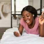 Cheerful Black female listening to music on bed. Photo credit: Unsplash