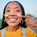 A black woman applying sunscreen to her face. Credit: Yuri Arcurs/Dreamstime.com