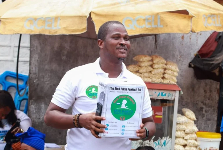 Ishmeal Alfred Charles holds a donation box in Sierra Leone asking passersby to donate money to save a sick child.