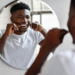A Black youth flossing his teeth in front of a mirror. Credit: Shutterstock