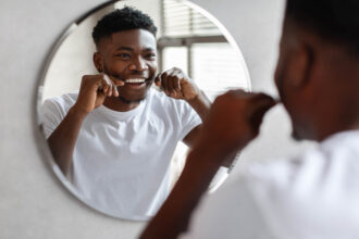 A Black youth flossing his teeth in front of a mirror. Credit: Shutterstock